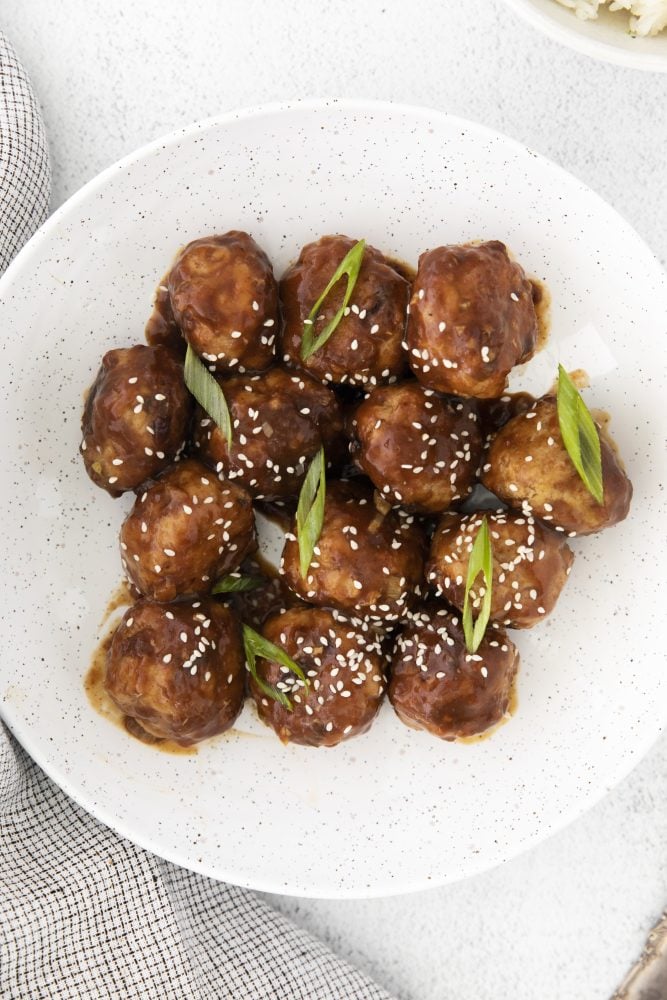 meatballs in sticky sauce with sesame seeds and green onions on it