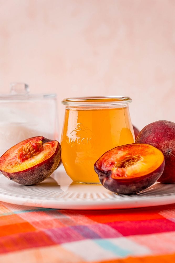 peaches cut in half next to a jar of peach syrup on a table