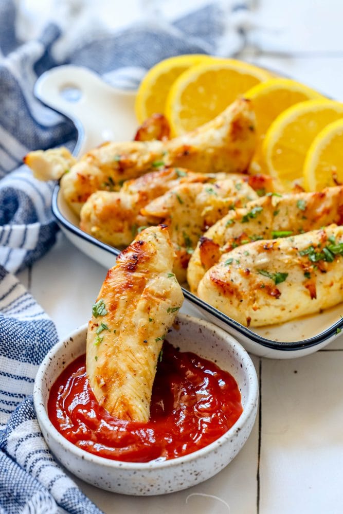 picture of naked chicken tenders in a white dish with lemon slices next to them
