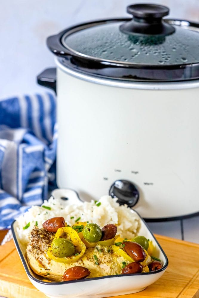 picture of chicken breast with olives and pepperoncinis in a white dish with rice in front of a slow cooker