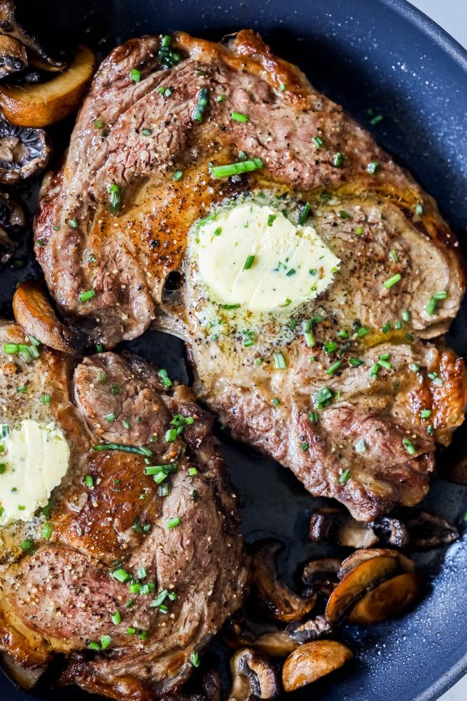 picture of ribeye steak with a pat of butter in a pan with mushrooms