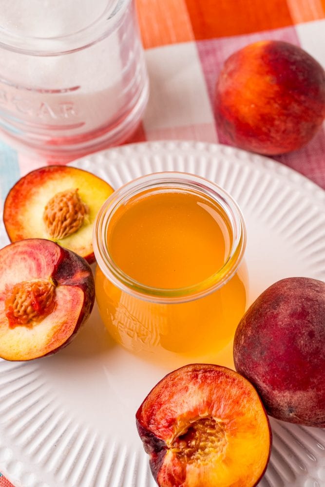 peaches cut in half next to a jar of peach syrup on a table