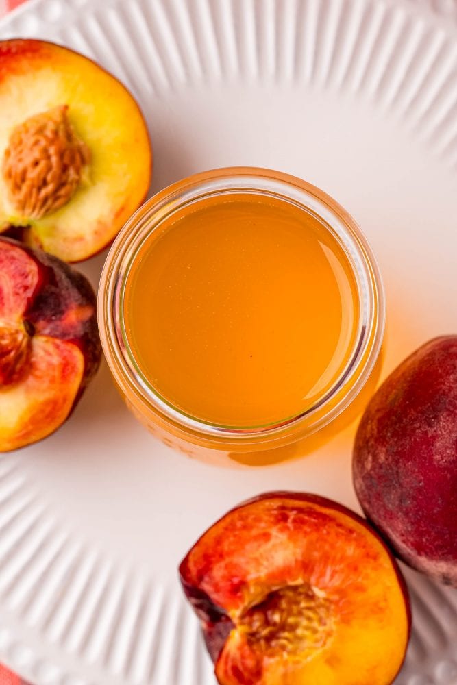 peaches cut in half next to a jar of peach syrup on a table