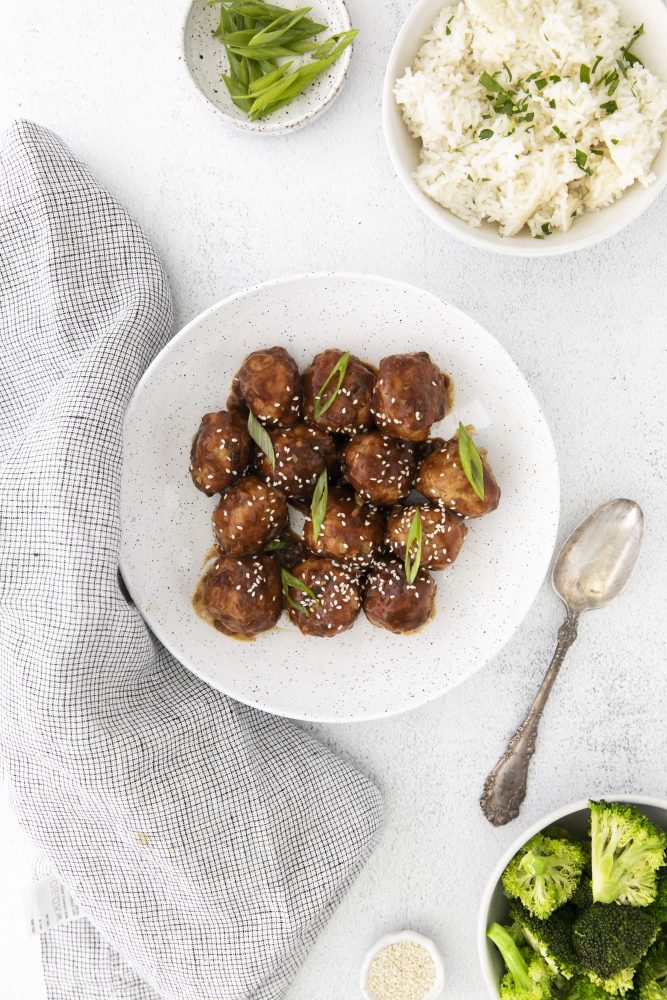 meatballs in sticky sauce with sesame seeds and green onions on it, bowl of rice