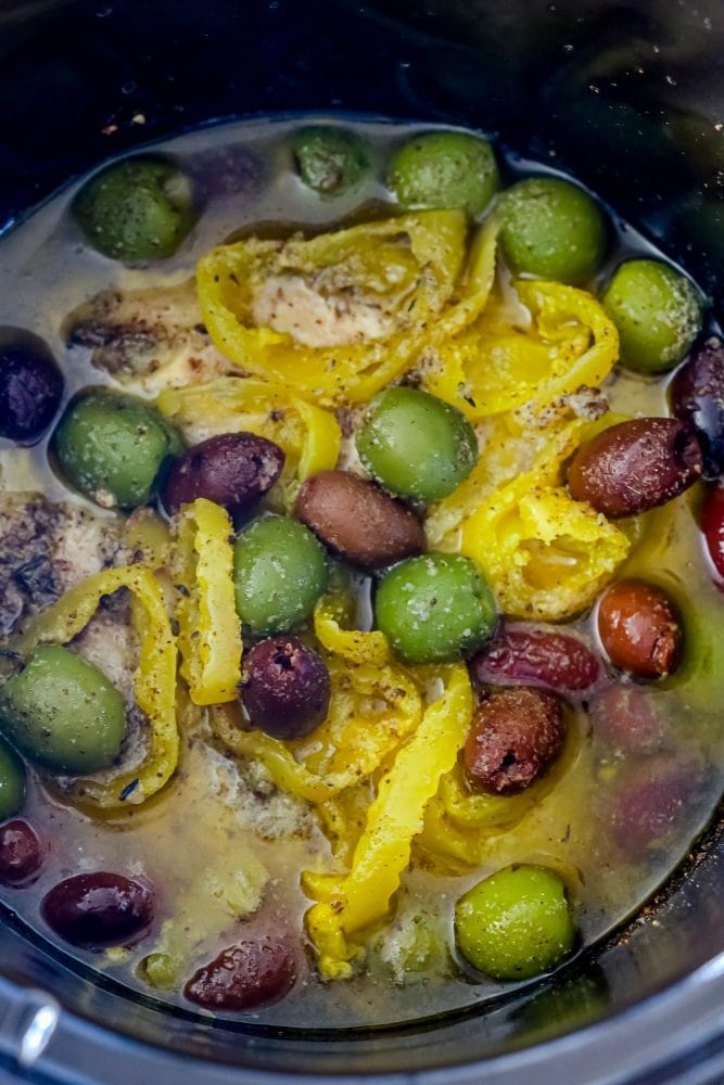 picture of chicken breasts in slow cooker with olives and banana peppers on top 
