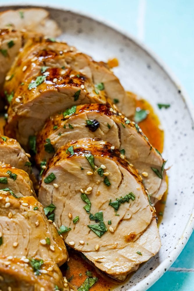 sliced pork tenderloin in teriyaki sauce with sesame seeds on top 