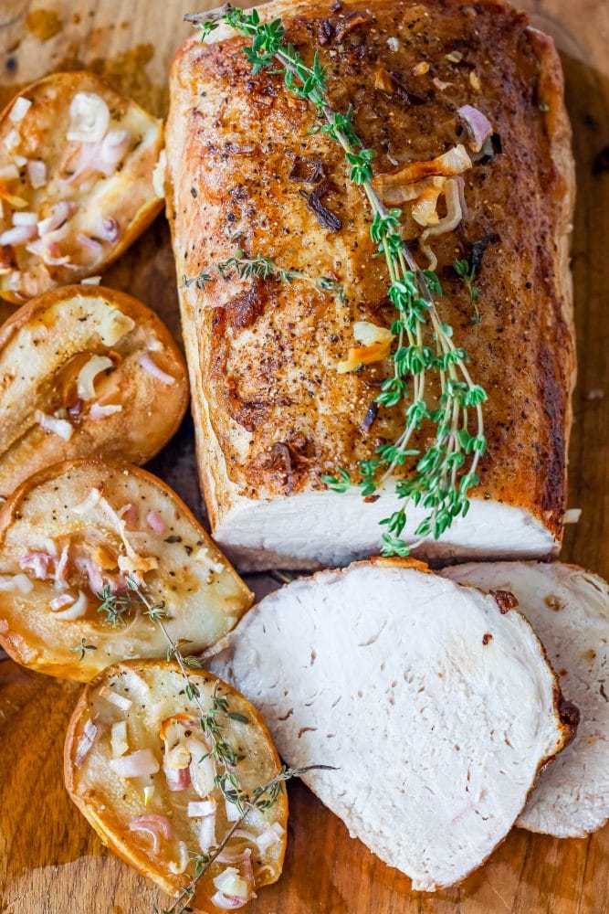 pork loin on a cutting board with roasted pears, shallots, and rosemary