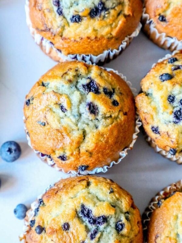 The Very Best Blueberry Muffins Recipe presented on a white plate with blueberries.