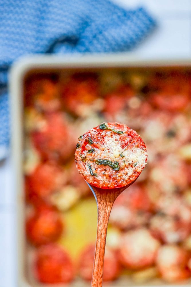 tomatoes in a casserole dish with garlic, basil, and parmesan cheese one on a wooden spoon