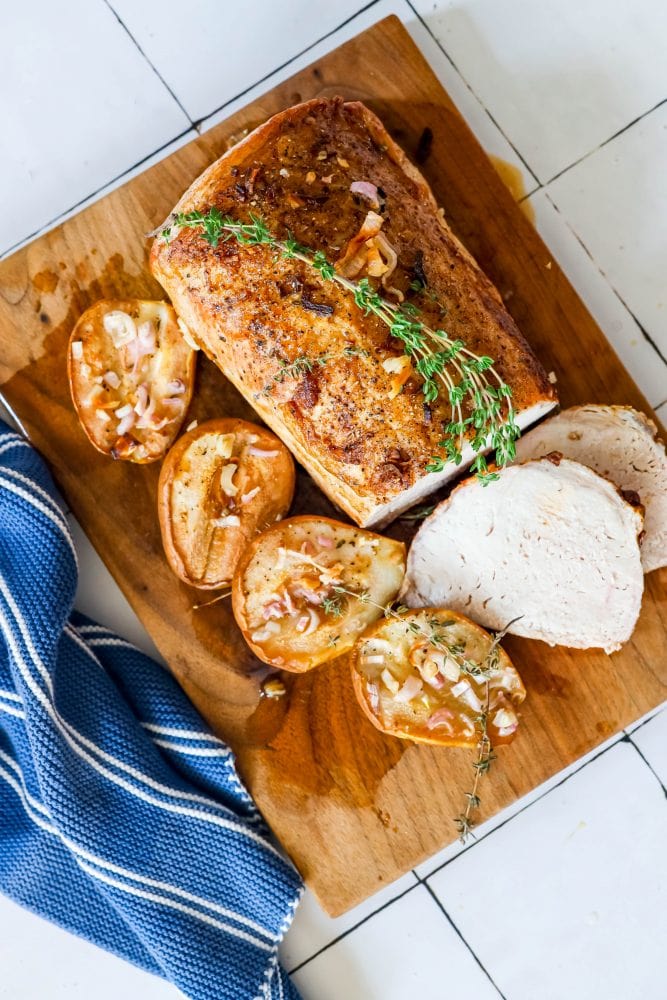 pork loin on a cutting board with roasted pears, shallots, and rosemary