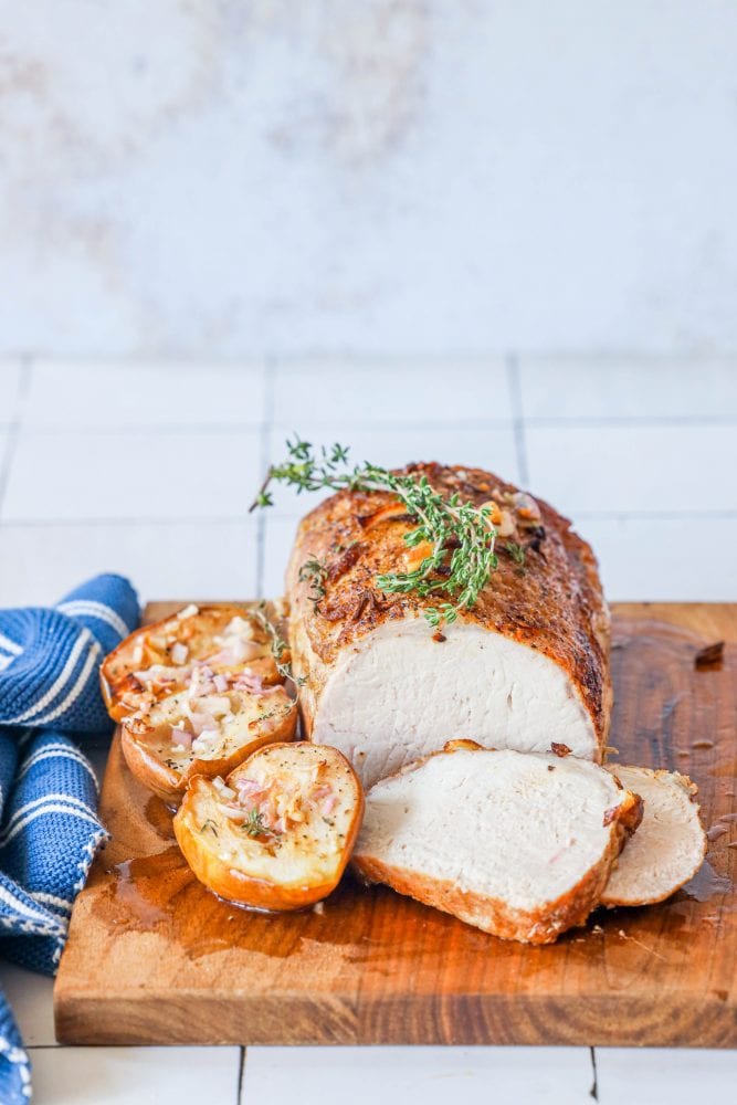 pork loin on a cutting board with roasted pears, shallots, and rosemary