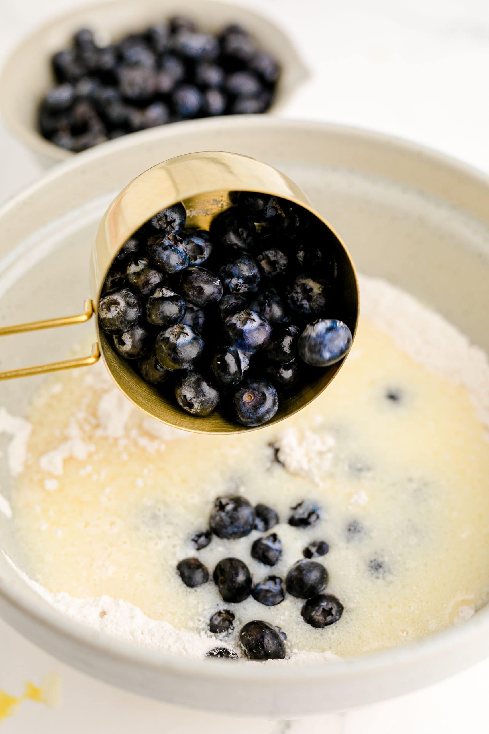 A blueberry recipe is being prepared by adding blueberries to a bowl of flour.