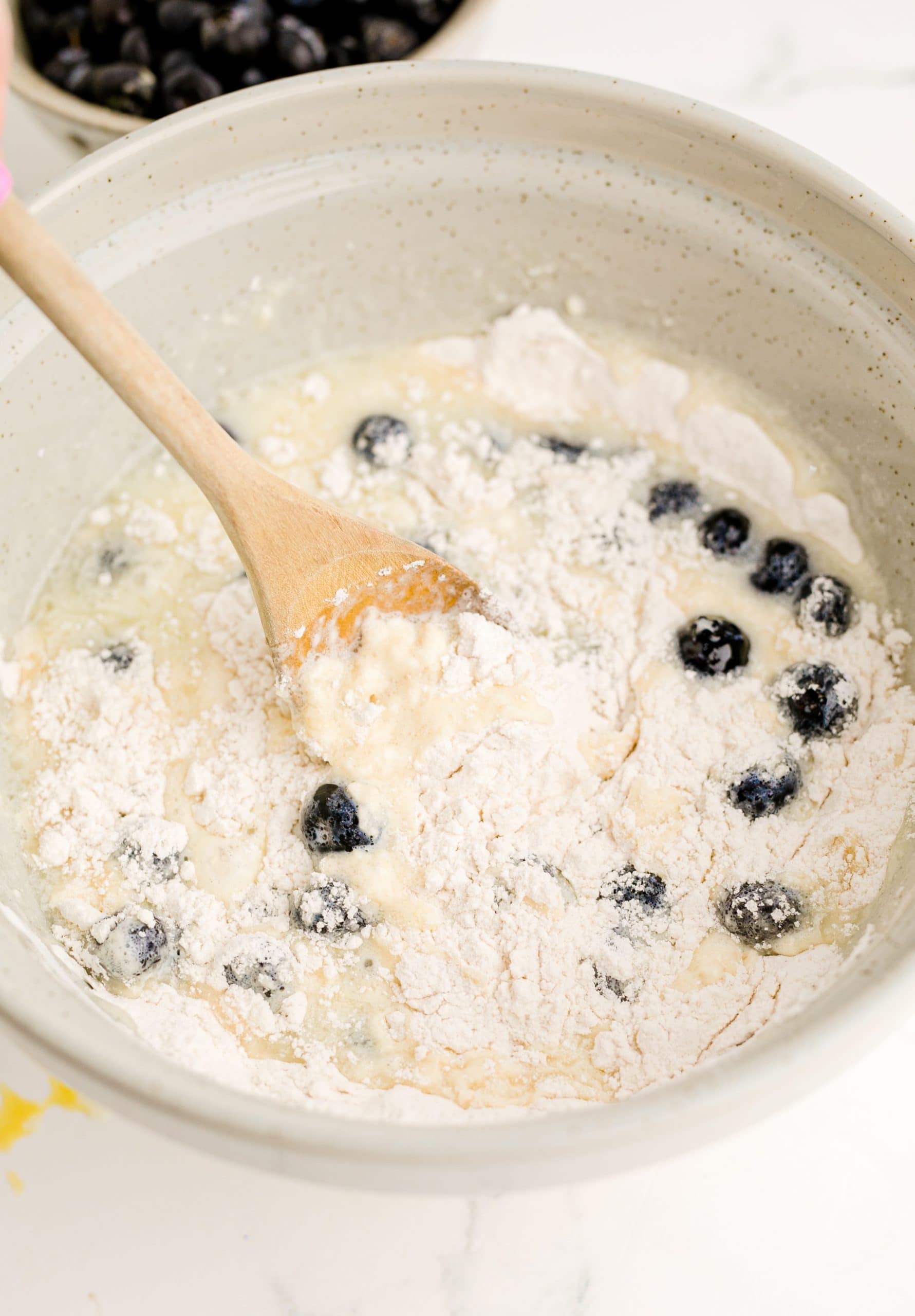 Blueberry pancake batter in a bowl with a wooden spoon.