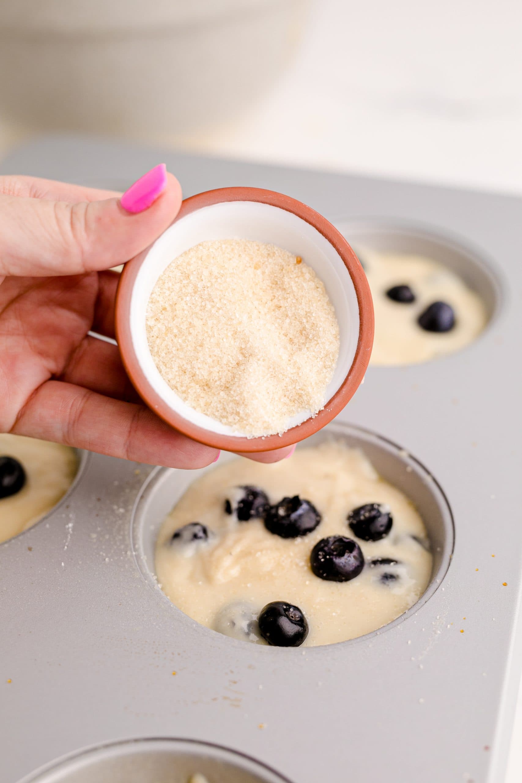 A person preparing jumbo blueberry muffins by pouring fresh blueberries into a muffin tin.