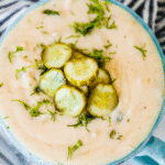 A close-up of a creamy pickle soup garnished with sliced pickles and chopped fresh herbs in a blue bowl—a delicious twist on the classic dill pickle soup recipe.
