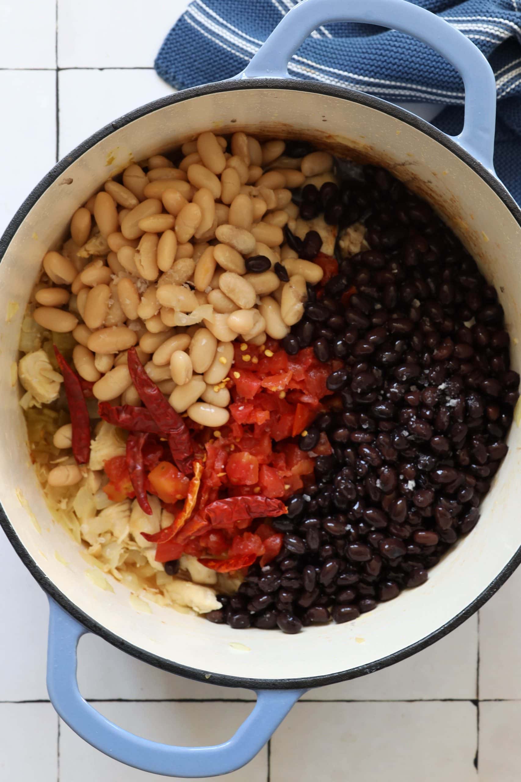 picture of diced chicken, ro-tel, green chilies, beans, dried chilies, and browned onions in a dutch oven pan