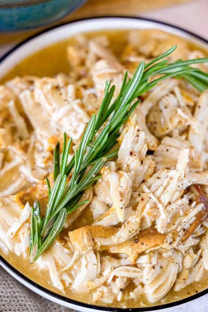 picture of shredded turkey in a slow cooker with gravy and a sprig of rosemary