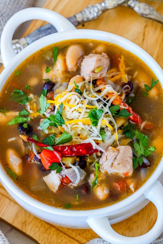 white bowl of soup with chicken, peppers, beans, cheese, and cilantro