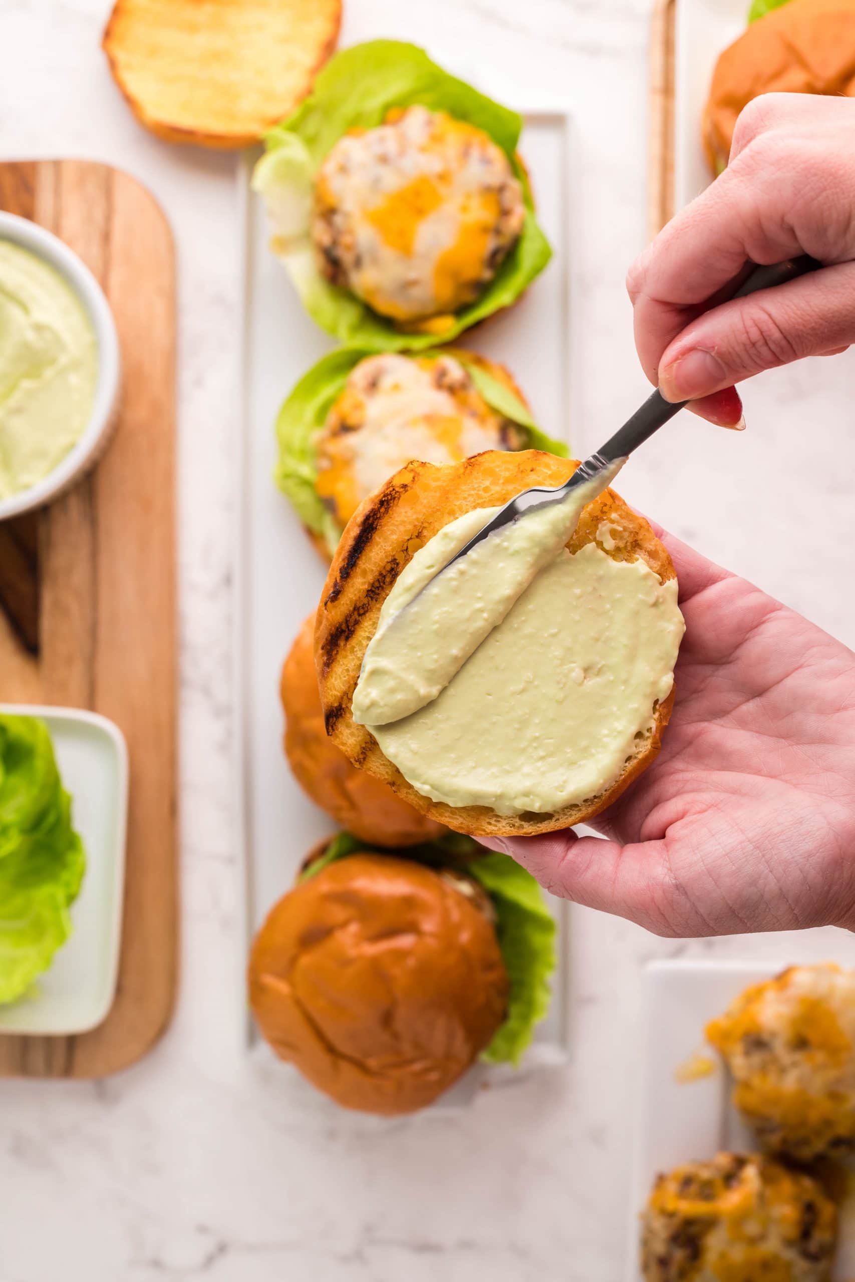 A person is dipping a spoon into a bowl of guacamole while making easy ranch turkey burgers.