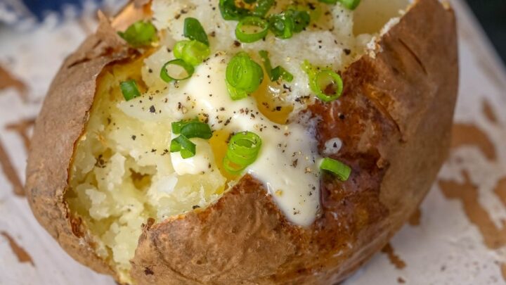 picture of baked potato with a pat of butter and chives on a wood cutting board