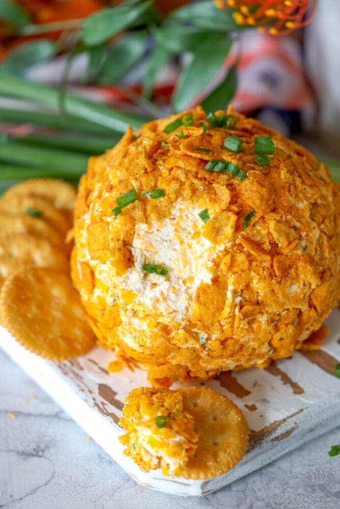 picture of cheese ball covered in crushed chili cheese fritos on a wood cutting board with crackers next to it 