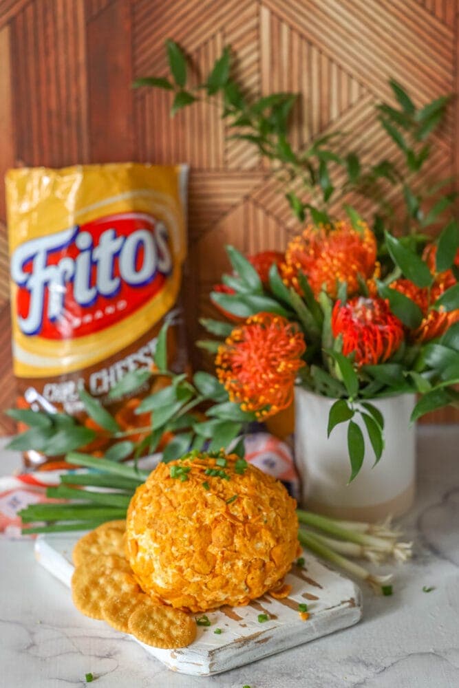 picture of cheese ball covered in crushed chili cheese fritos on a wood cutting board with crackers next to it 