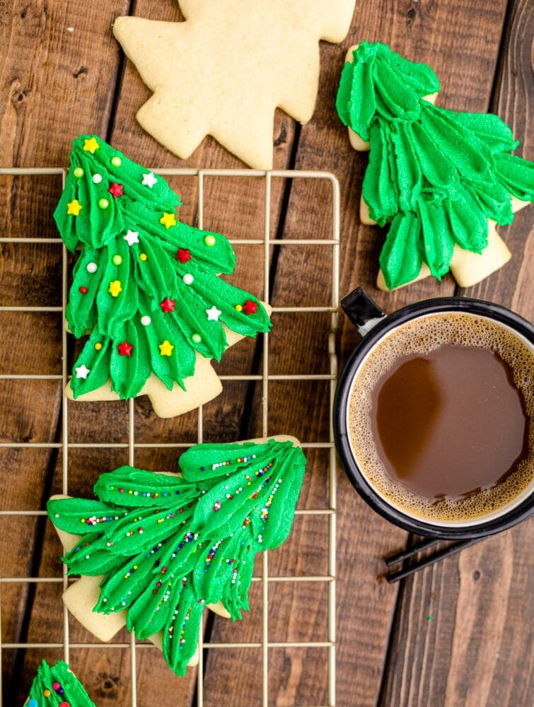 picture of iced christmas tree sugar cookies on a cooling rack next to a cup of coffee