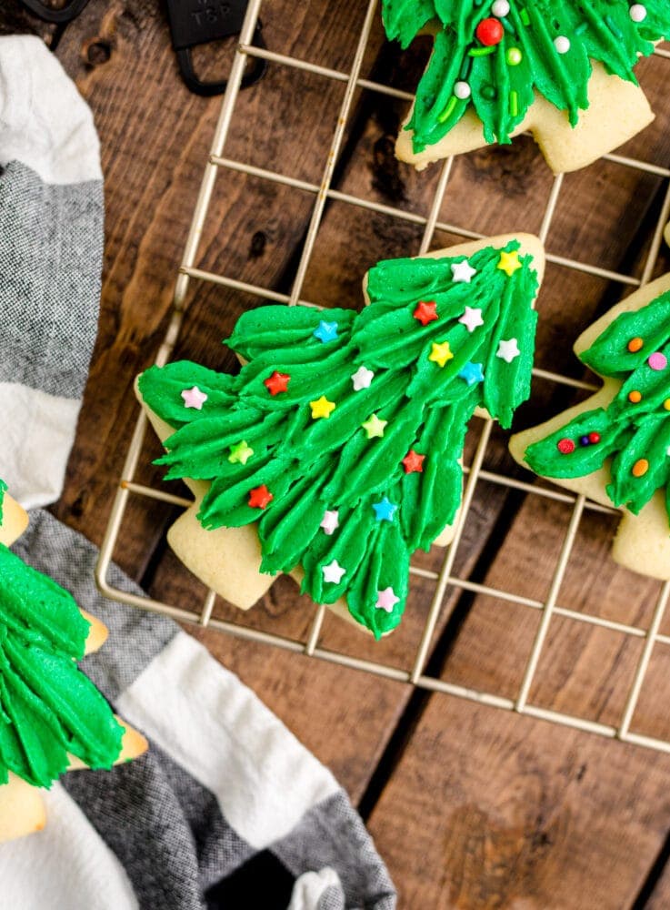 picture of iced christmas tree shaped cookie with sprinkles on a cooling rack 