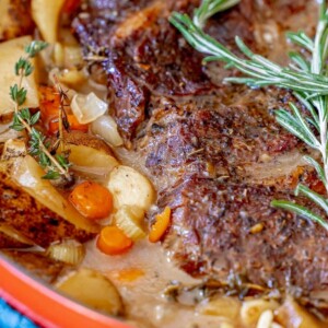 picture of pot roast in a dutch oven with vegetables and rosemary on top