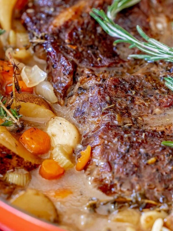 pot roast in a dutch oven with vegetables and rosemary on top
