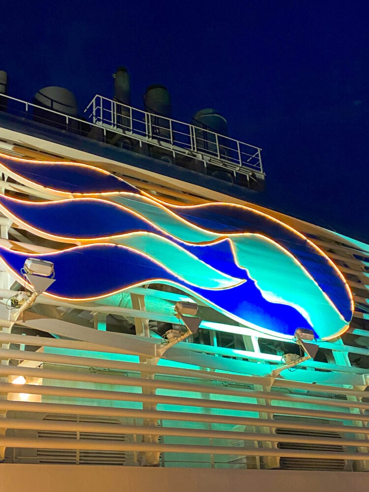 picture of the Princess Cruises logo lit up on the side of the Majestic Princess ship at night 