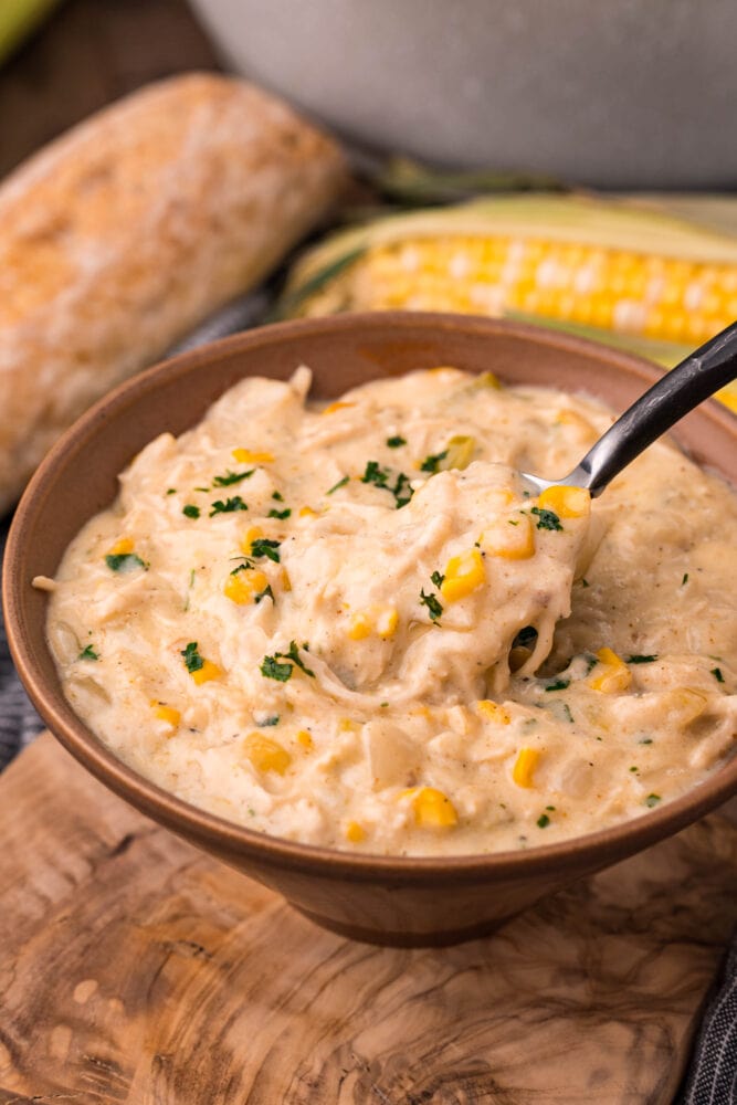 picture of a spoon scooping up a spoonful of corn chowder with shredded chicken in a bowl