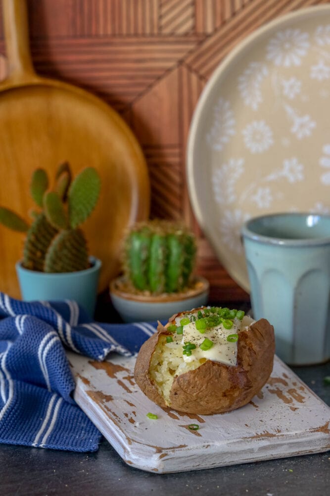 picture of a baked potato on a wood cutting board with butter and chives on top 