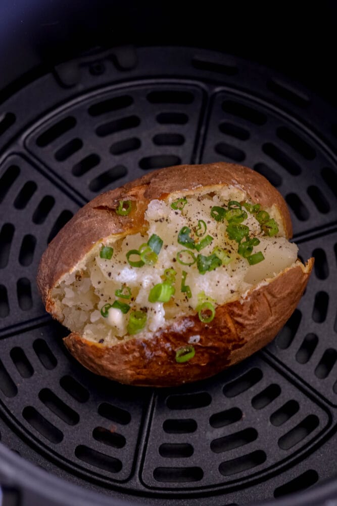 picture of a baked potato in an air fryer with butter and chives on top 