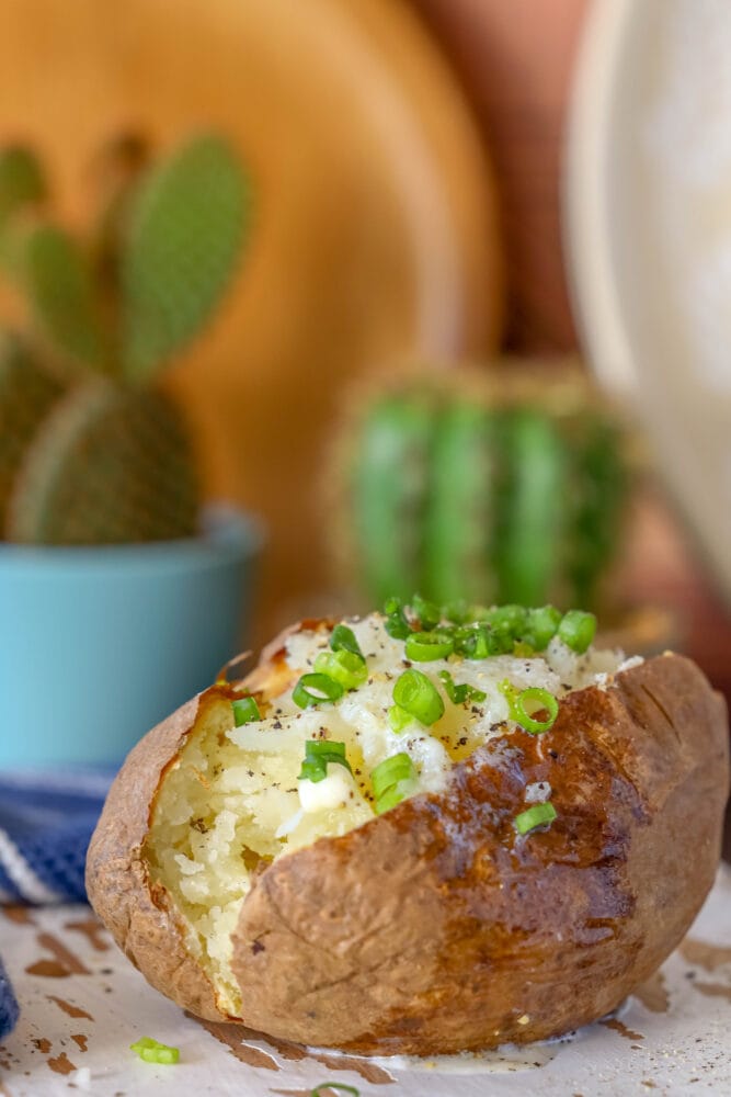 picture of a baked potato on a wood cutting board with butter and chives on top 