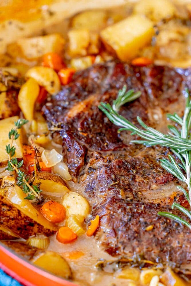 picture of pot roast in a dutch oven with vegetables and rosemary on top