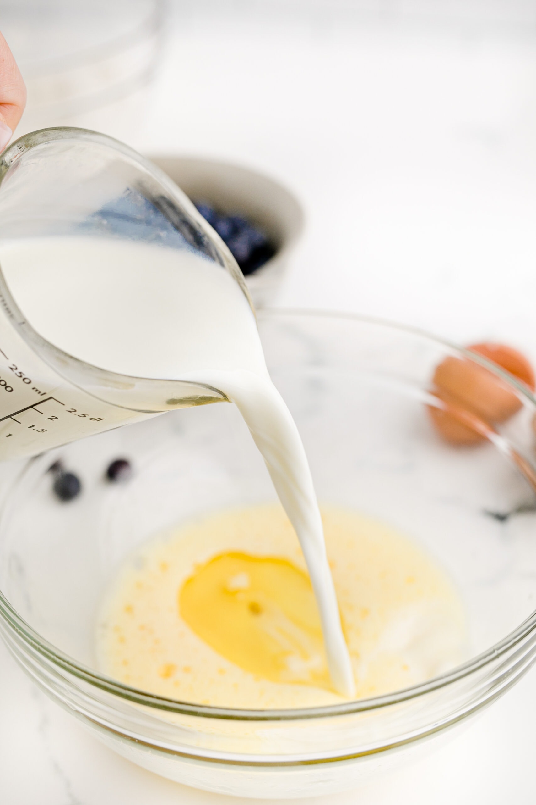 A person pouring milk into a bowl of ingredients.