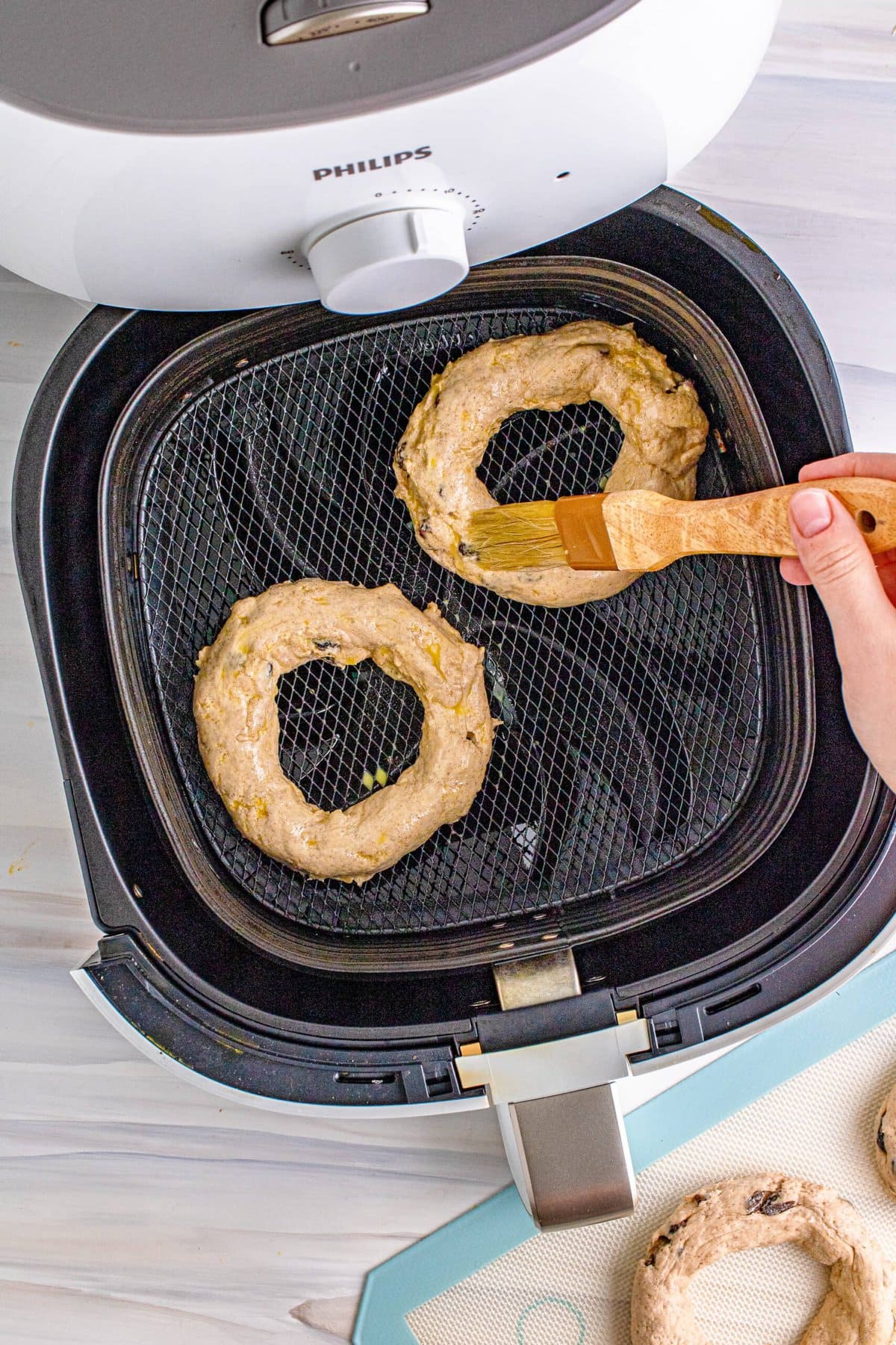 A person holding an air fried cinnamon raisin bagel in front of an air fryer.