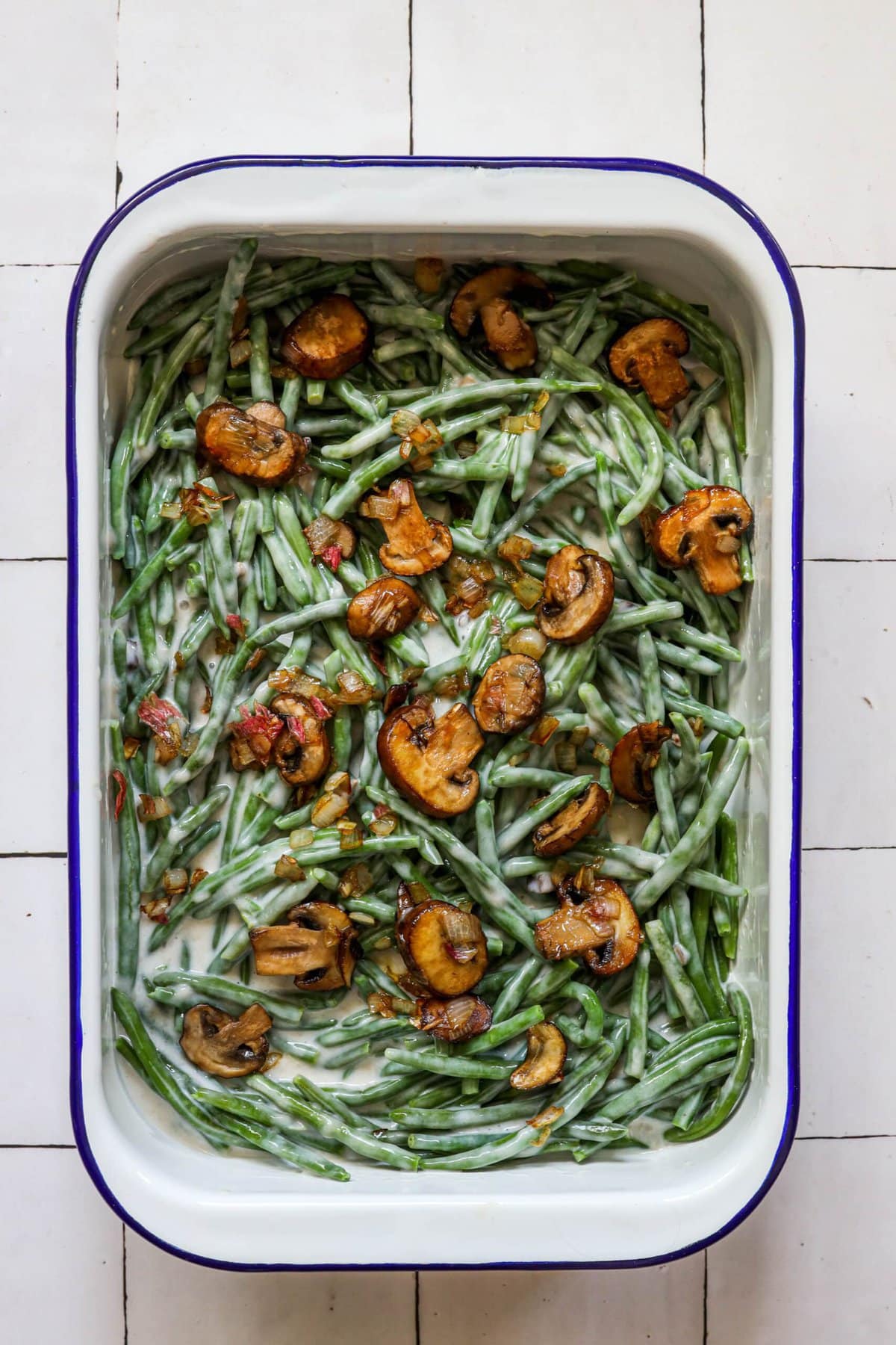 picture of green beans in a baking dish with cream, milk, and mushrooms on top