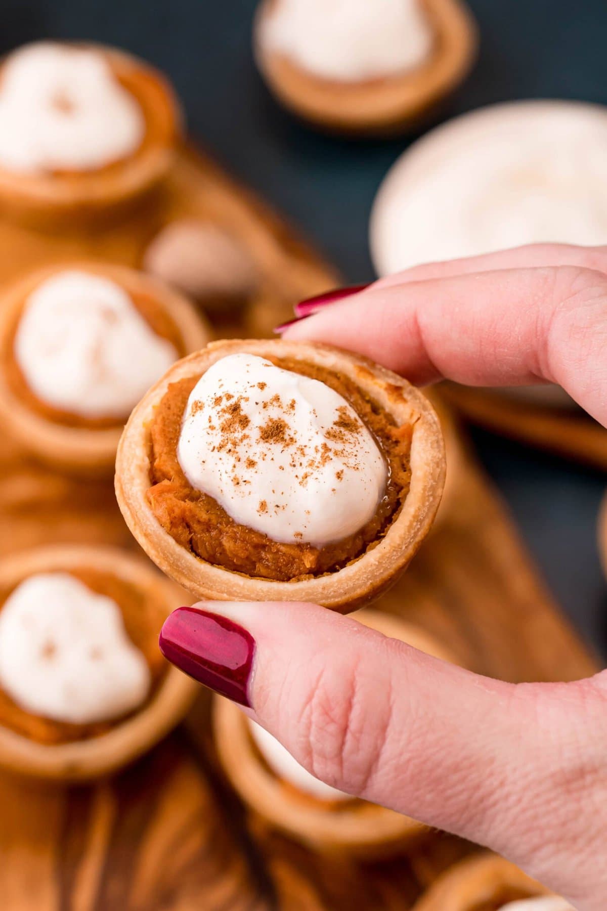 A hand holding a pumpkin pie topped with whipped cream, perfect for your sweet potato pie recipe.