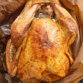 Roasted whole turkey on brown parchment paper, seasoned and cooked using the Brown Bag Herb Roasted Turkey Recipe to achieve a perfect golden-brown hue.