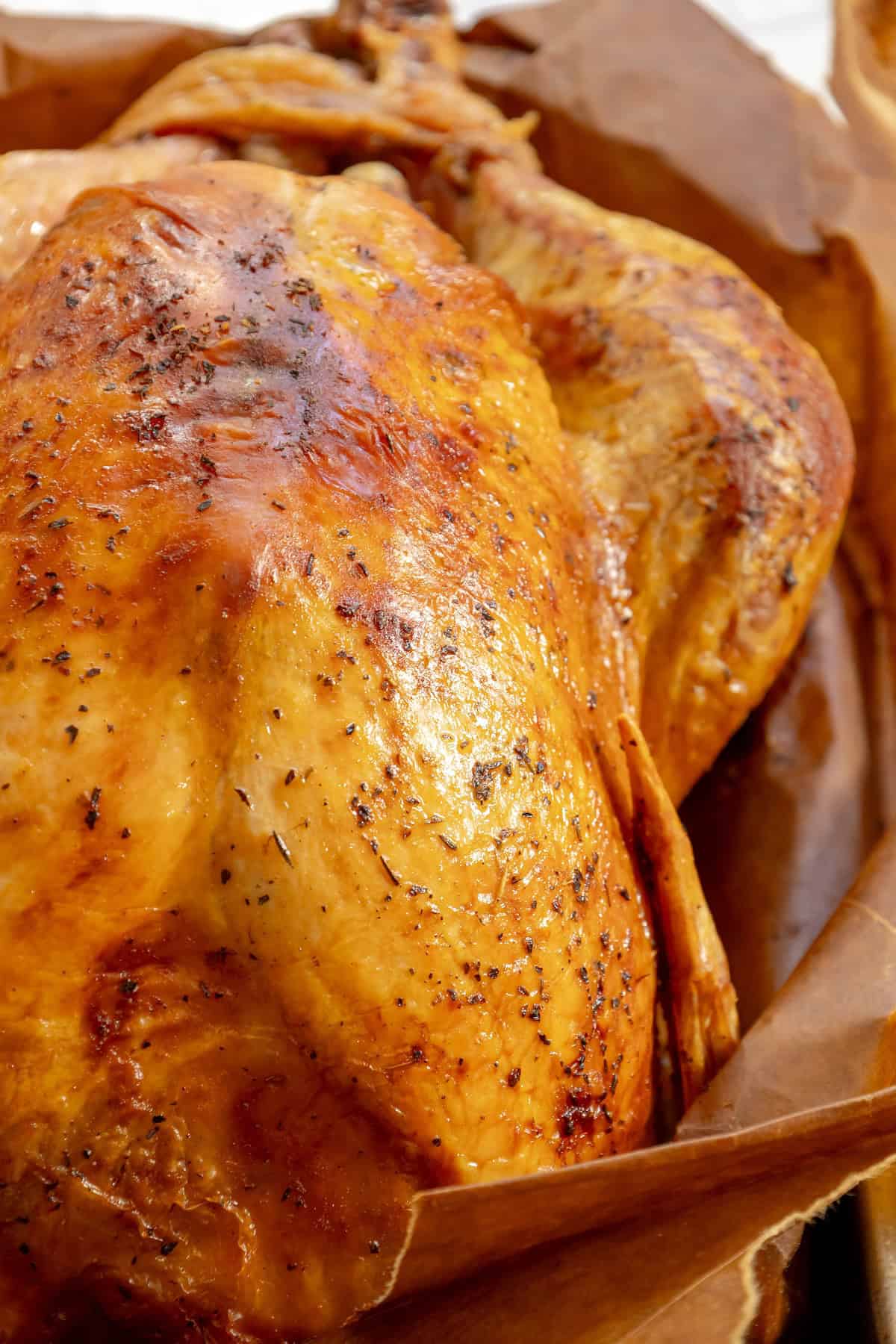 Close-up of a golden-brown roasted chicken resting on parchment paper, reminiscent of the crispy skin and rich seasoning you'd find in the easiest way to cook turkey using a classic brown bag method.