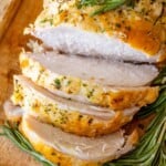 Oven Baked Turkey Breast with rosemary sprigs on a wooden cutting board.