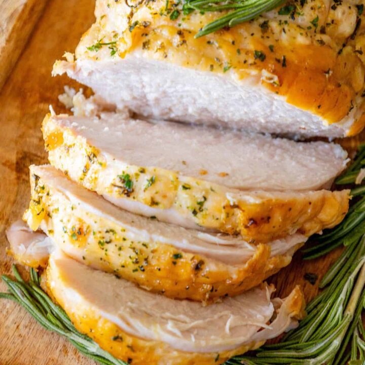 Oven Baked Turkey Breast with rosemary sprigs on a wooden cutting board.