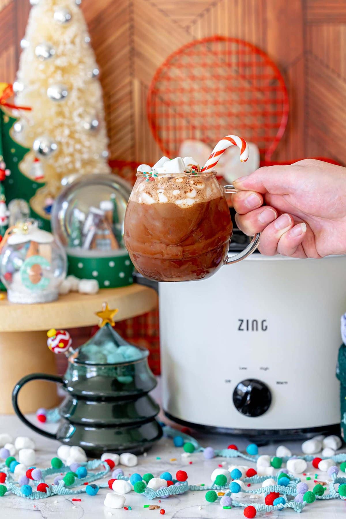 Rich and Creamy Slow Cooker Hot Chocolate 13 A person holding a warm mug of homemade slow cooker hot cocoa in front of a beautifully decorated Christmas tree, embodying winter coziness.