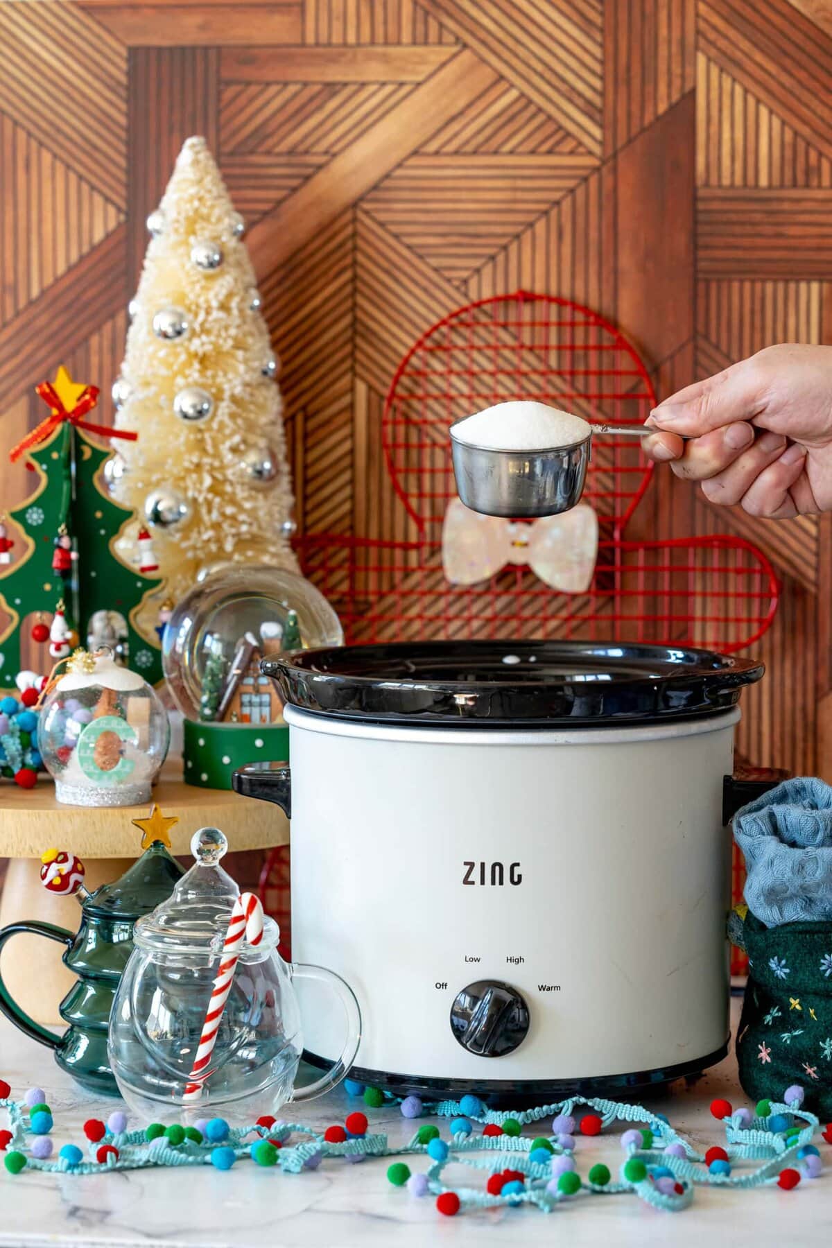 Rich and Creamy Slow Cooker Hot Chocolate 8 A hand adding granulated sugar to the slow cooker, contributing to the sweetness of the homemade hot chocolate.