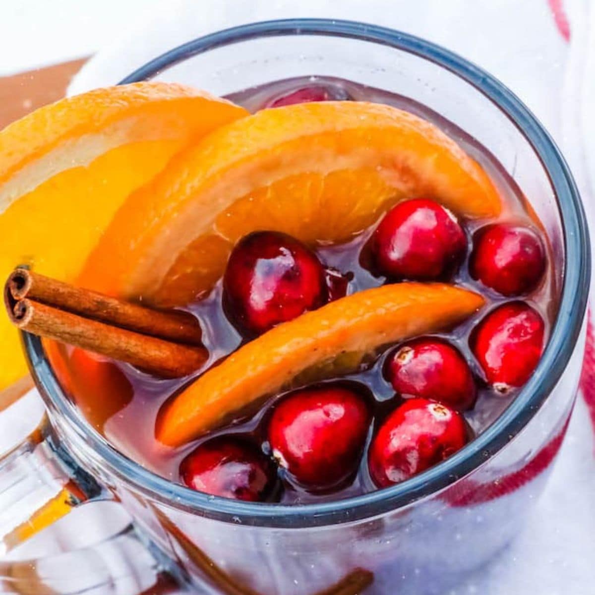 mulled wine in a clear mug with cranberries, cinnamon, and orange slices floating in it