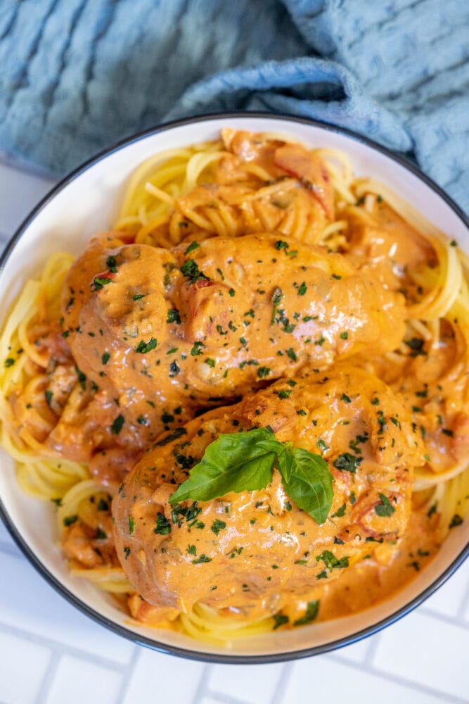 picture of creamy tomato basil chicken breasts in a bowl over pasta