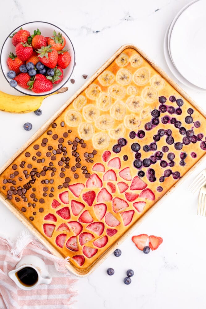 Picture of a sheet pan of a pancakes topped with fruit and chocolate chips next to a bowl of fresh fruit 
