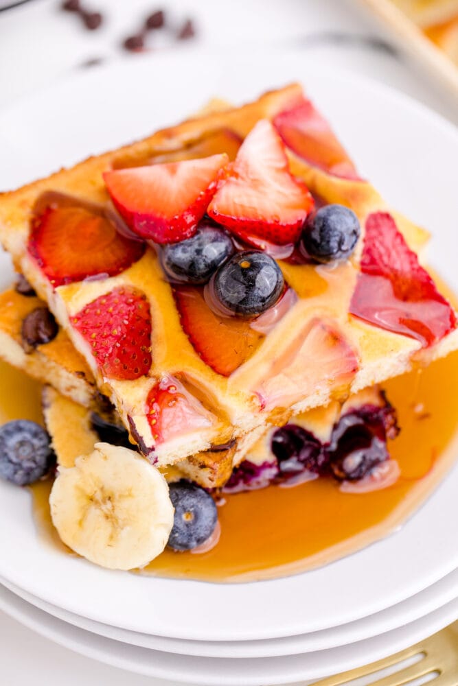 A picture of a stack of pancakes with syrup and fruit on top 